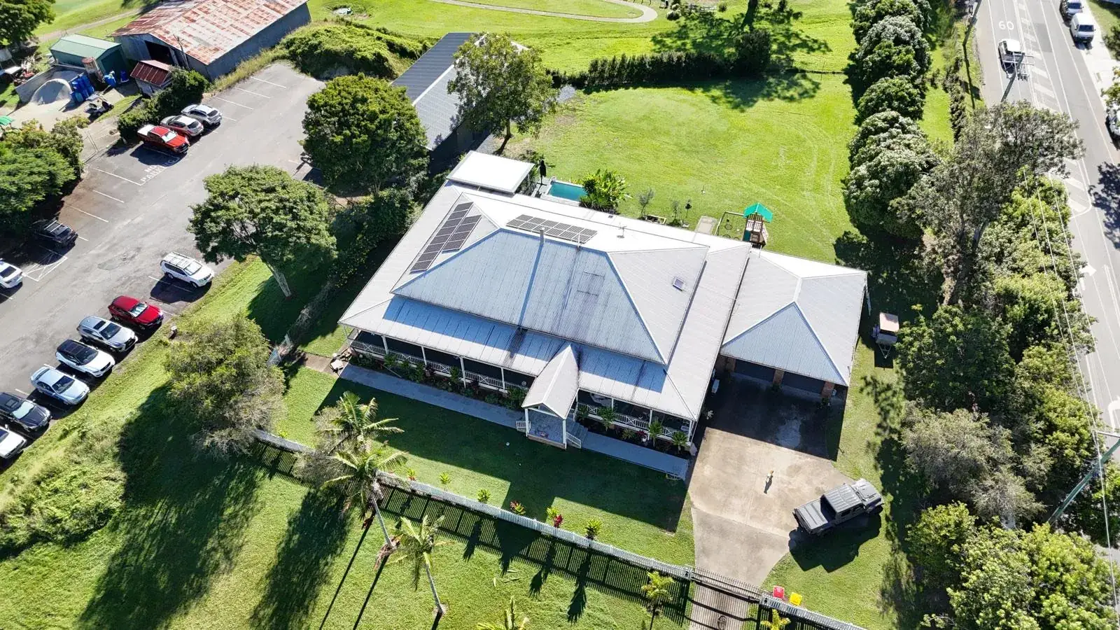 Aerial photograph of a large silver metal roof on a Queenslander-style building beside a road